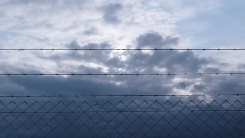 I walk along the fence with barbed wire, there are gloomy clouds in the sky and the sun has disappea