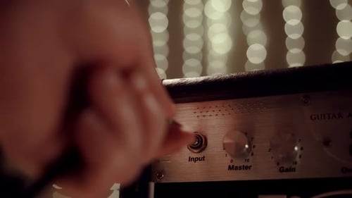 A Man Turns the Volume Knob on an Electric Amp to Guitar Close Up