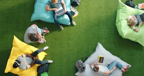 Above view of students using modern technology and sitting on bean bags at campus