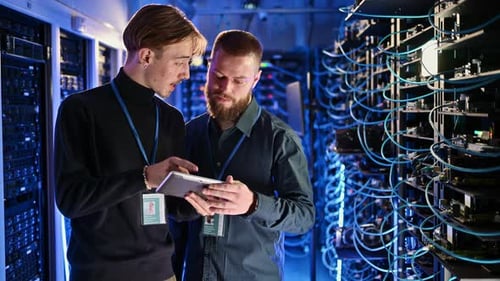 System Engineers Collaborate in Server Room with Tablet