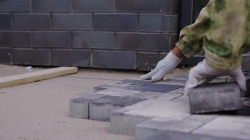 Worker Laying Concrete Paving Blocks on Sand Base During Installation