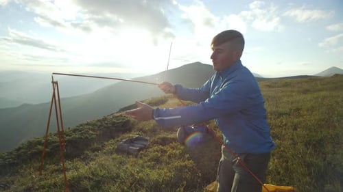 Young Adult Assembles Tent on Grassy Mountain