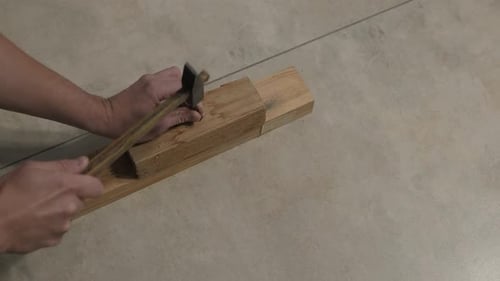 Man hammering nail into wood planks indoors