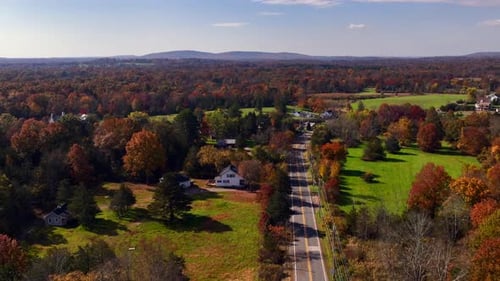A high angle aerial view over the quiet countryside of New Jersey with colorful trees and large gree
