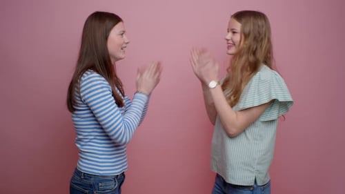Mädchen spielen das Klatschspiel auf rosafarbenem Hintergrund