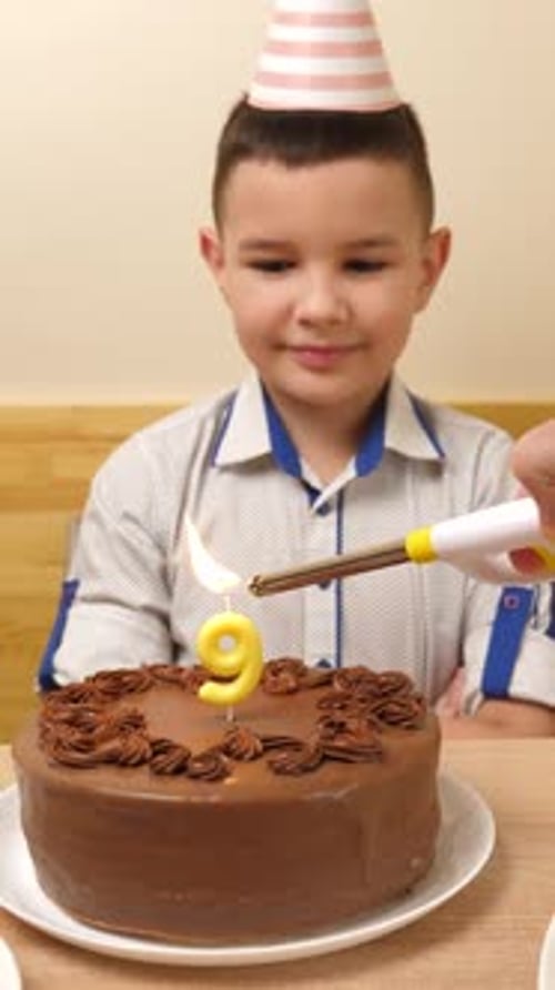 08. The boy is sitting in front of a table with a festive cake, in which a candle in the form of the
