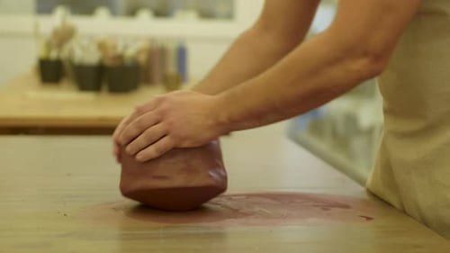 Male hands rolling raw clay block on workshop table top preparing project