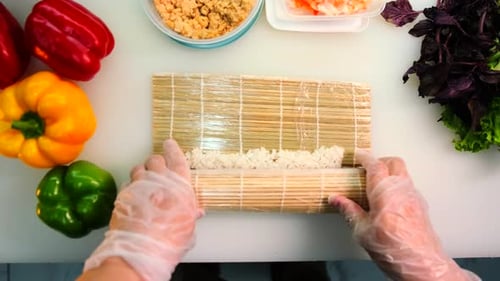 Vista de cima, chef de sushi embrulhando um pãozinho usando uma esteira de sushi de bambu na mesa da cozinha