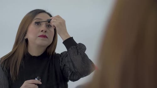 Woman with brown hair applying mascara to eyelashes, wearing black long sleeved top using a large