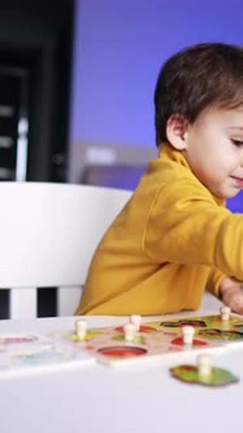 Baby boy in yellow sweater reaches for a puzzle piece. Toddler kid playing with puzzles at home.