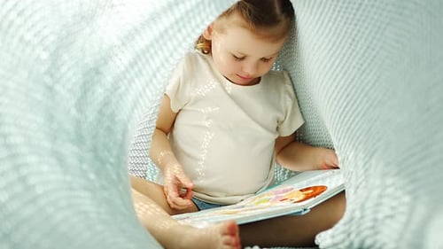 Little Girl Enjoying of Review a Book Under Blue Knitted Plaid in Sunny Morning