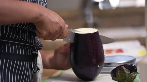 Black, African American hands slicing a large, whole eggplant in half - isolated slow motion