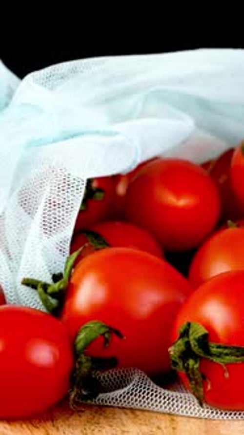 Apila jugosos tomates cherry frescos en una bolsa de malla ecológica que gira suavemente
