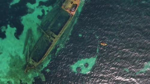 Man in a kayak explores the sunken wreck of the Michelle ship in the clear sea in summer. Drone view