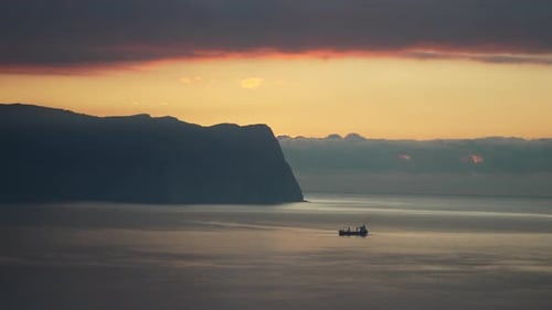 Cargo Ship Ocean Sunset Vessel Sails Peacefully Near a Towering Coastal Cliff During a Calm and