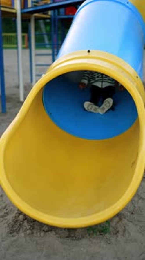 Lovely child appears from the tunnel slide. Smiling kid stands on his feet and runs to slide again.