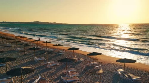 Aerial drone shot of a tropical beach at sunset. View of the wooden umbrellas and sun beds at the be