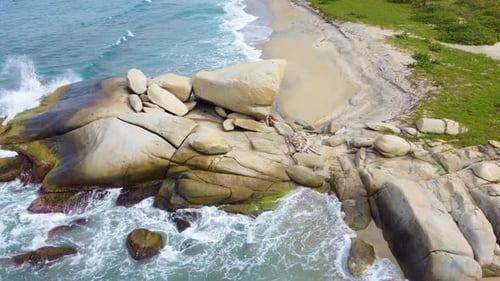 Drone descending view of water waves crashing against large rock. Santa Marta Colombia, Tayrona Natu