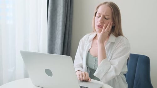 Woman with Headache Sitting at Laptop in Home