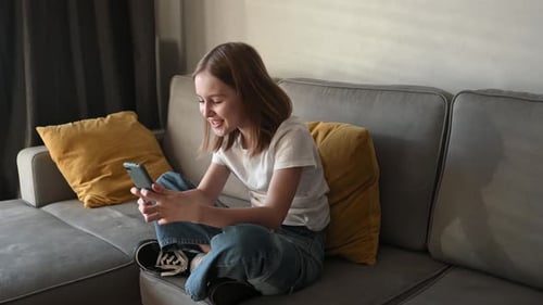 Girl Using Mobile Phone Sitting on Couch Smiling