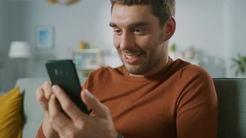 Young Man Happily Using Mobile Phone on Sofa