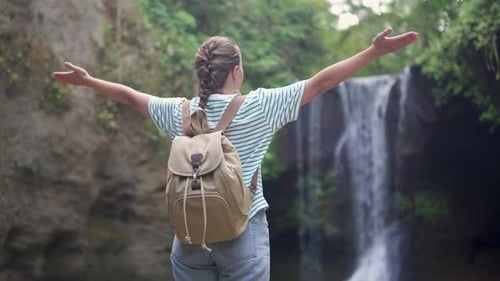 Female tourist with backpack is enjoying view of a waterfall