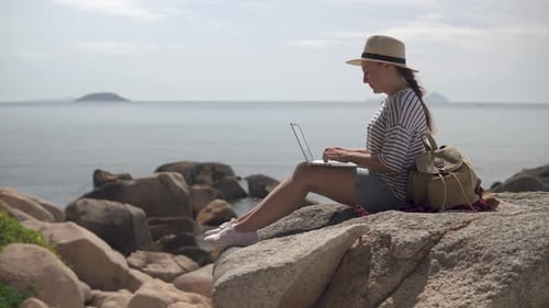 Woman Using Laptop Sitting on Rocks by Ocean
