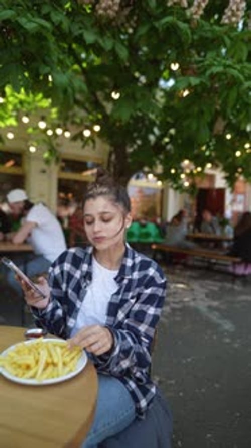 With the Summer Sun Shining a Girl is Relishing French Fries on a Café Terrace
