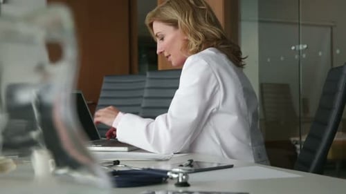 Blonde Woman Doctor Works on Laptop in Office