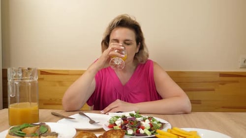 Woman at Table Pours Orange Juice and Eats Salad