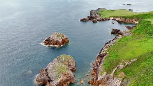 Green grass covering the rocks at the waterscape. Some bare boulders stick out form water.