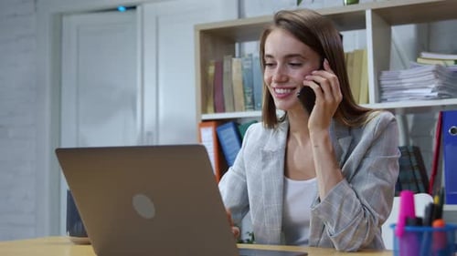 Young Woman Working on Laptop and Talking on Phone