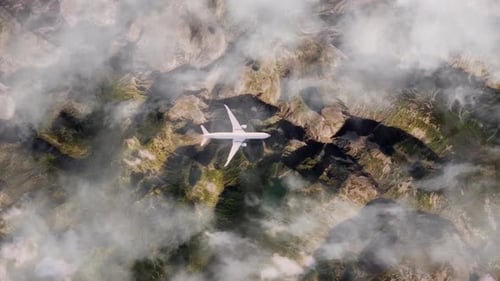 Aerial View of Airplane Flying High Above Rugged Mountain Terrain and Clouds