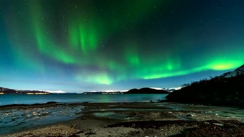 Timelapse view from Norwegian arctic beach as green aurora borealis dance in sky