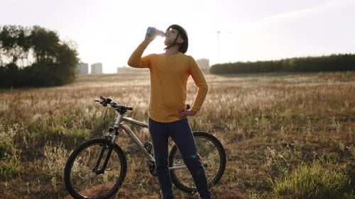 Radfahrer trinkt Wasser beim Stopp auf dem Feld nach dem Radfahren bei Sonnenuntergang