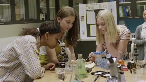 Female Junior High Teacher and Girl Students Conducting Scientific Experiment at Microscopes 1213 Ye