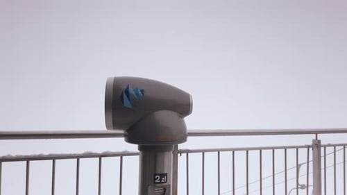 Snowy observation deck telescope spinning on pedestal looking out at ski resort cable car scenery