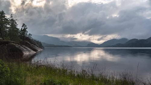 De sombres nuages orageux tourbillonnent au-dessus du lac avec ses rives rocheuses et ses montagnes.