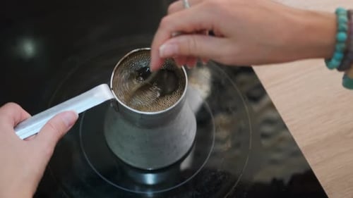Hands of a Young Woman Stirring Bubbling Hot Coffee with a Spoon