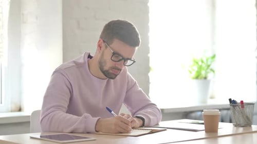 Young Man Writing on Paper in Office