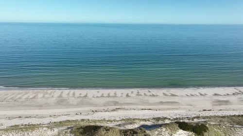 A serene cape cod beach with calm ocean waves and clear skies on a sunny day, aerial view