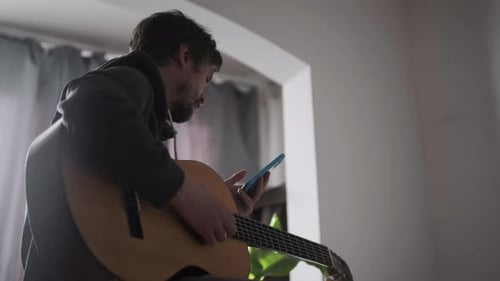 Man Playing Guitar and Using Smartphone Indoors