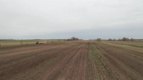 Aerial view from drone flying low over farm field as tractor moves in opposite direction. Organic fa