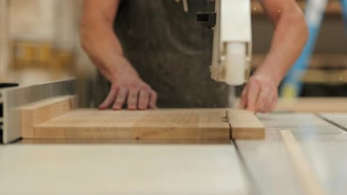 Craftsman using table saw to cut wood for a project in a workshop during daylight hours