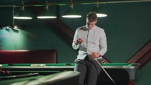 Young Player Sitting on Pool Table Holding Cue Stick with Focused Expression