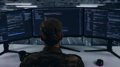 Asian Military Using Computer To Write Code With Multiple Screens In Data Center