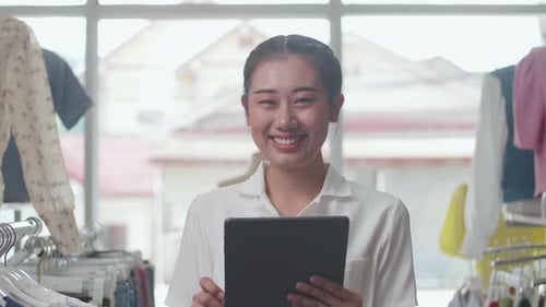 Close Up Of Asian Female Owner Of Clothing Store Smiling To The Camera While Using Digital Tablet