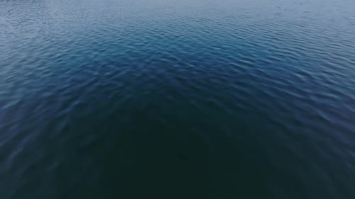 High Angle View of Water Surface Forwards Fly Above Lake Tilt Up Reveal City and Mountains in