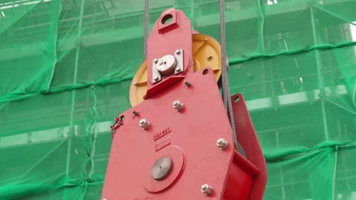 Close Up Of Tower Crane Hook Block At Work. Scaffoldings In Background.