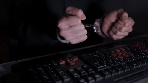 Handcuffed Hands Over Keyboard in Dark Room